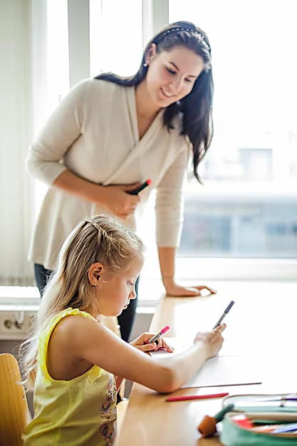 Insegnante che segue una bambina mentre scrive al banco